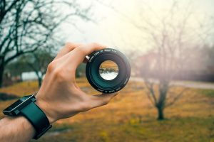 mans hand holding a camera lense awareness