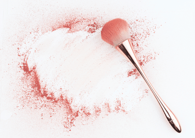 Image of a makeup brush on a white surface surrounded by blusher powder.