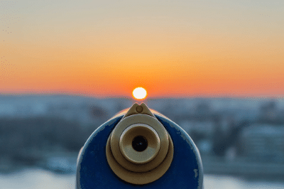 Photo of the lens end of a scope with a cityscape at sunset in the background