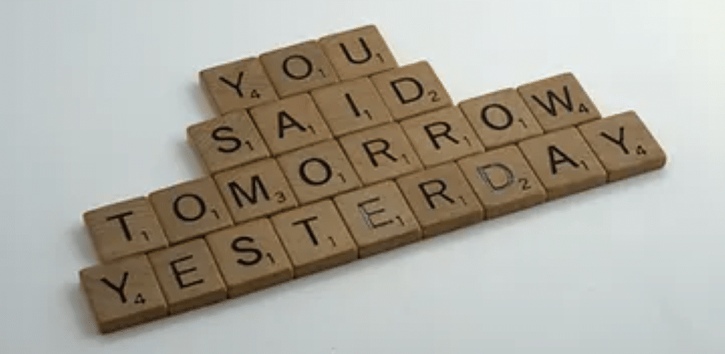 Photo of Scrabble game pieces on a white surface, ordered so they spell out 'You said tomorrow yesterday'.