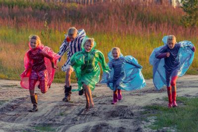 Photo of a group of children in colourful waterproofs happily running down a muddy track