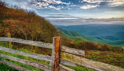 Outdoor scene of rolling green hills, with low cloud in the far distance, and a wooden fence in the foreground.